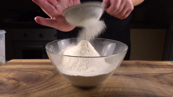 Sifting flour through a sieve into a glass bowl in the kitchen