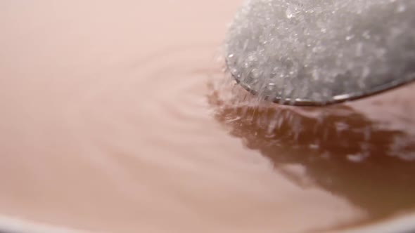 Adding sugar to coffee. Crystals pour from a full spoon into the drink in slow motion