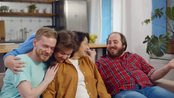 Happy Senior Mother and Adult Children Hugging Sitting on Couch at Home