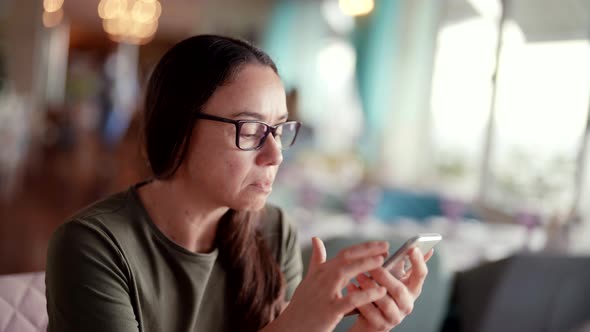 Closeup of a Successful Businesswoman with Glasses Using the Phone While Sitting in a Cafe at