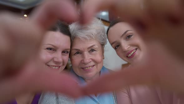 Closeup Female Hands in Heart Shape with Smiling Adult Senior and Young Women Looking at Camera