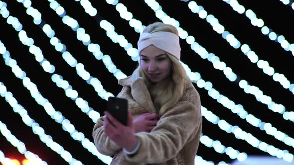 The Girl Takes a Selfie Against the Background of Christmas Lights Against the Backdrop of the