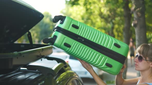 Young Woman Driver Taking Out Green Suitcase From Car Roof Rack on City Street