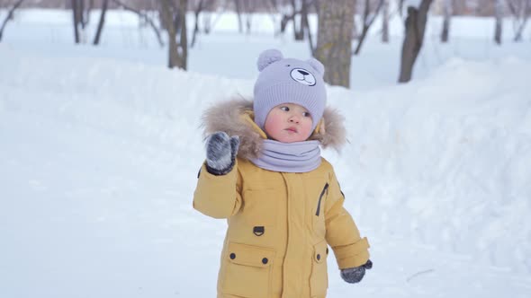 Toddler 12-17 months old greets by waving his palm in a winter park