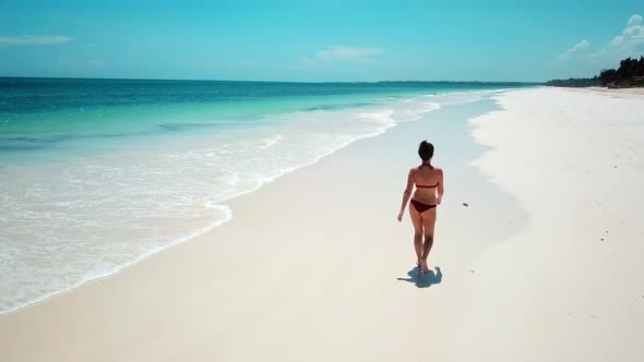 Rear View Of A European Woman Wearing Swimwear, Walking On White Sand Beach Resort In Kilifi, Kenya.