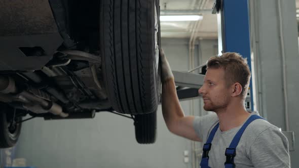 Car Mechanic Examining Car Suspension of Lifted Automobile at Repair Service Station Man