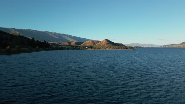 Wide blue Clutha river with lush green hills at the river bank. Low dolly aerial view of blue river