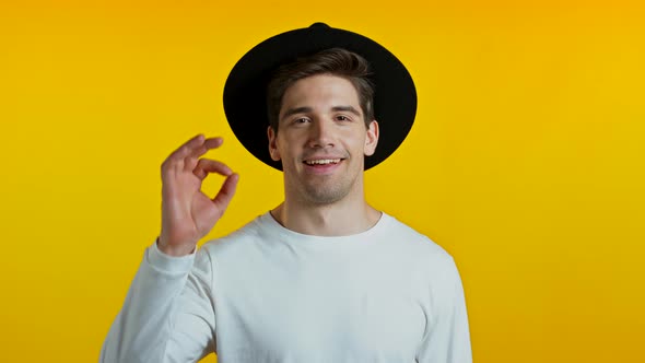 Handsome Young Man in White Shirt Smiles To Camera. Hipster Guy Showing OK Sign Over Yellow