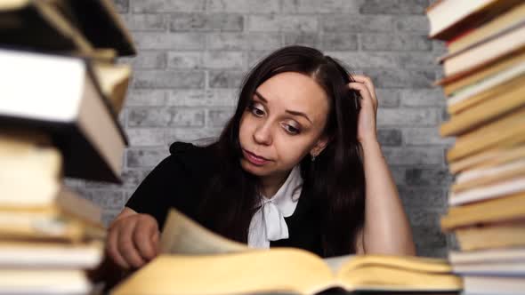 Tired Female Student Reading Among Books. Pensive Young Woman Sitting at Table with Pile of Book and