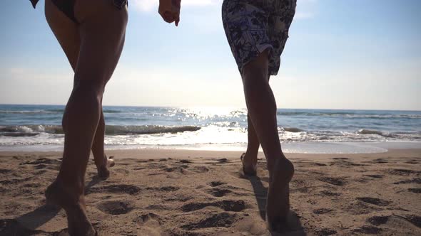 Young Happy Couple Running on the Beach to the Sea and Holding Hands of Each Other