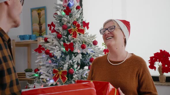 Happy Senior Couple Enjoying Christmastime Sharing Wrapper Gift Present in Xmas Decorated Kitchen