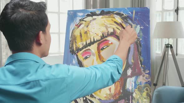 Asian Artist Man Holding Paintbrush Mixed Colour And Painting A Girl's Hair On The Canvas