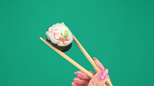 Female Hands Hold Japanese Chopsticks with Sushi Rolls on Green Background