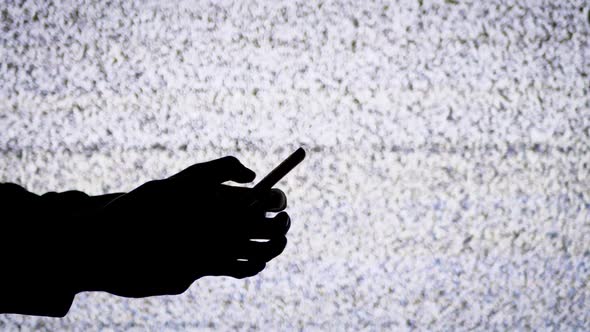 Silhouette of a Hand Holding a Smartphone on TV Screen Background with White Static Noise