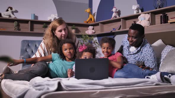 Happy Family Using Laptop Chatting Online on Bed