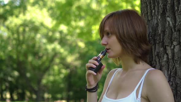 Young Girl Smokes Vape in the Park