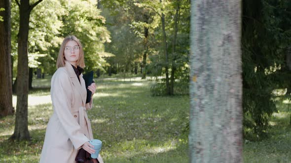 Young Girl Walks in the City Park on a Sunny Autumn Day Wearing a Coat