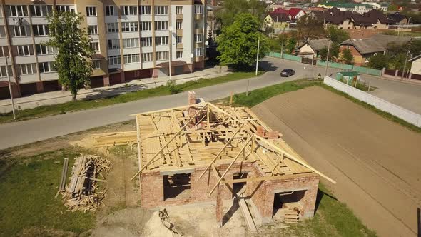 Aerial view of unfinished brick house with wooden roof frame structure under construction.