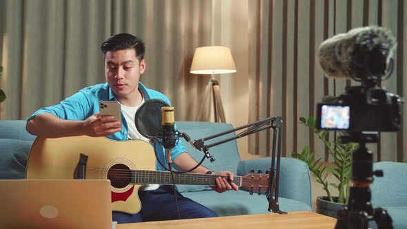 Asian Man Is A Vlogger With Guitar Read Comment On Mobile Phone. The Male Is Streaming