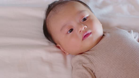 An Asian newborn baby is laying down on a soft white sheet mattress. Starring at his parents and fee