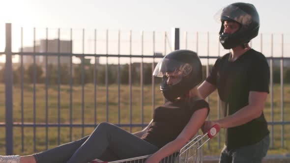 Guy Rolls Attractive Young Woman in the Trolley in Motorcycle Helmets at Sunset