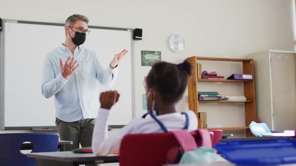 Caucasian male teacher wearing face mask teaching students in the class at school