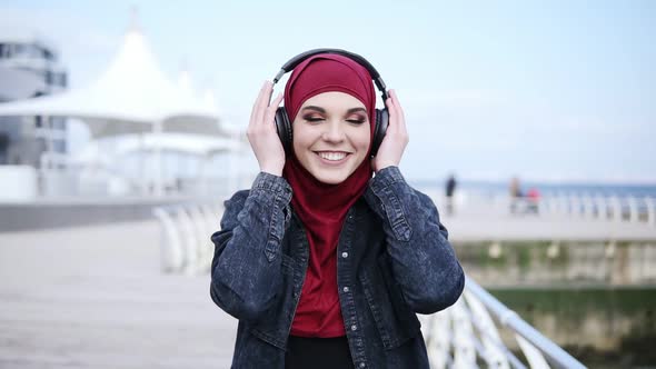 Slow Motion Footage of a Young Attractive Girl with Hijab on Her Head Putting Headphones on Smiling