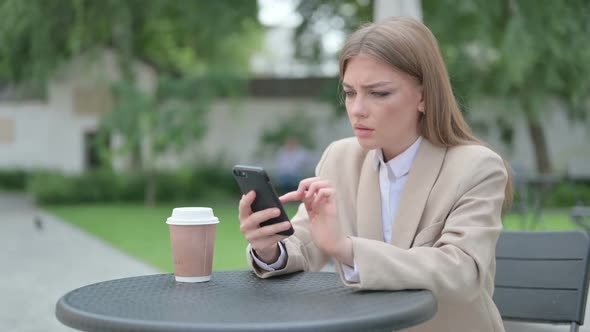 Young Businesswoman Reacting to Loss on Smartphone in Outdoor Cafe