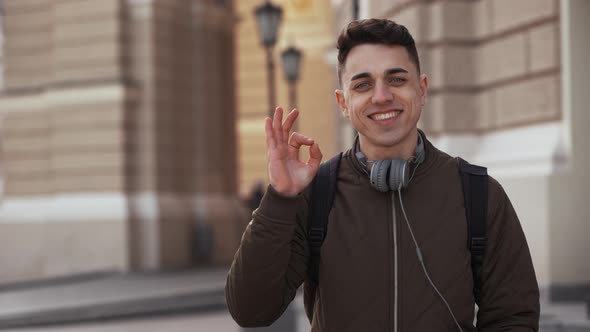 Portrait of Happy Attractive Guy 20s Wearing Backpack and Headphones Posing Over Old Historic