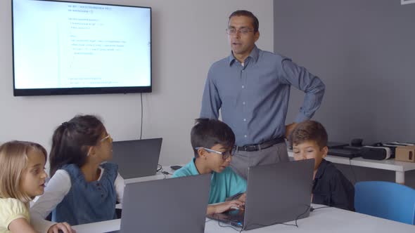 Teacher Watching Excited Classmates Using Laptops