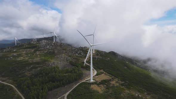 Mountain shrouded in clouds and slowly spinning wind turbines blades. Aerial orbit