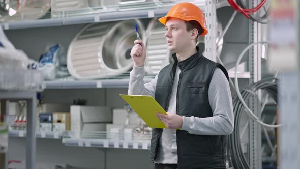 Confident Worker in Hart Hat Comparing Goods on Shelves with Supplies List