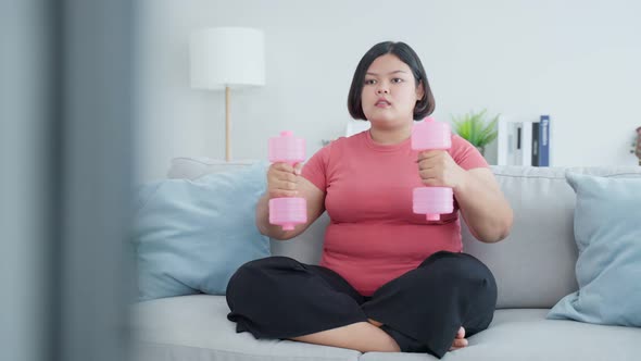 Asian young plus size girl use dumbbell workout exercise by follow gym instructions video at home.