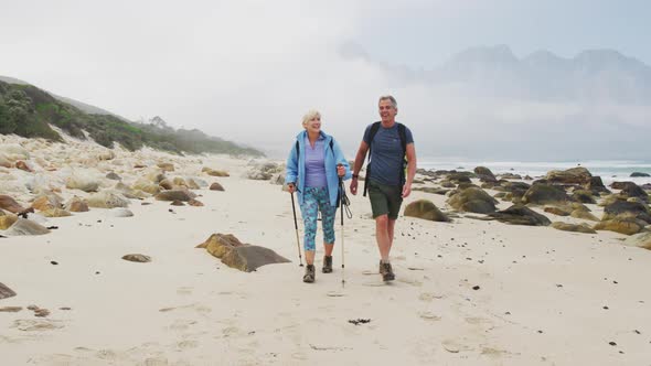 Senior hiker couple with backpack and hiking poles talking to each other and walking while hiking