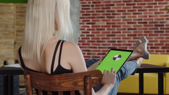 Woman is Sitting Chair with Her Feet on Table and Swipe Her Finger on Screen of Tablet with