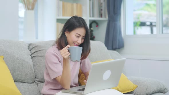Young business freelance Asian woman working on laptop checking social media and drinking coffee.