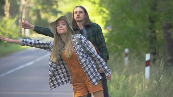 Millennial Tourist Happy Couple in Plaid Hipster Shirts Want To Catch Car Making Hitch-hiking Near