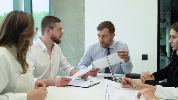 A Group of Young Male and Female Office Employees Sitting and Discussing on a Project in a