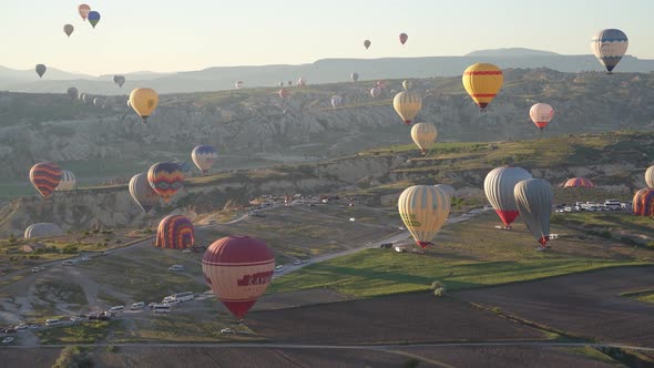 Hot air balloons fly over the mountainous landscape of Cappadocia, Turkey.