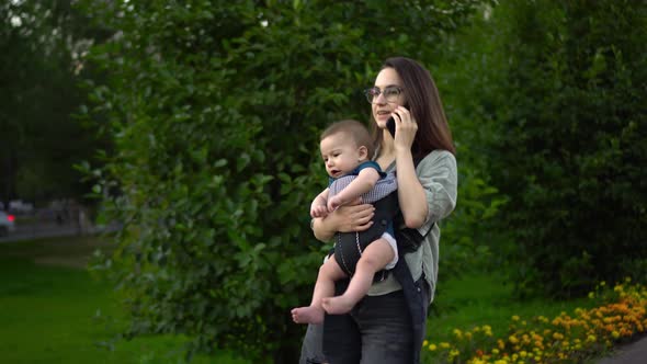 A Young Mother Walks in the Park with a Child and Speaks on the Phone