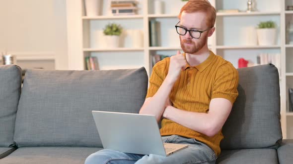 Redhead Man Thinking and Working on Laptop at Home