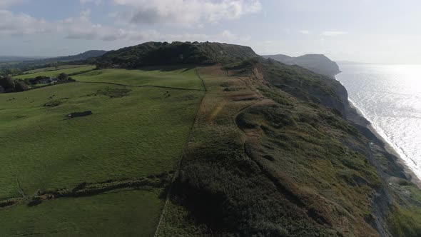 Golden cap and Charmouth beach cliffs are revealed with an aerial track from inland to out to sea lo