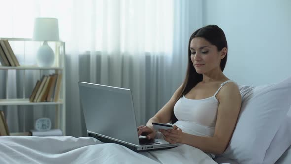 Smiling Lady Booking Hotel Online Using Credit Card, Planning Vacation in Bed