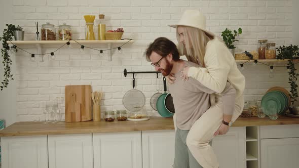 European Middleaged Bearded Man Having Fun and Lifting His Fiancee Piggyback in Their Modern Bright