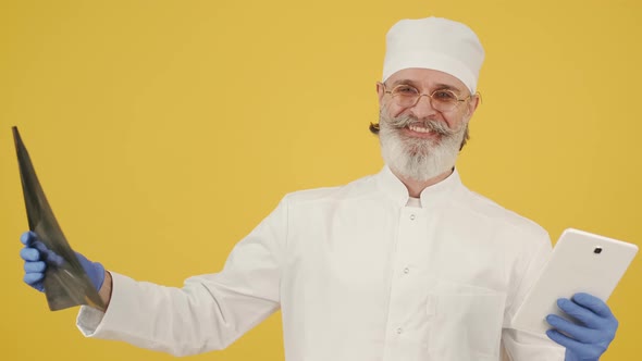 Male Senior Doctor Looking at X-ray Image on Yellow Background