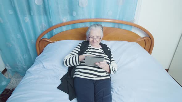 Senior Woman Scrolls Social Media Using Tablet PC on Bed