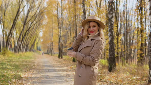 Young Woman in a Brown Coat and Hat Walks in the Autumn Park