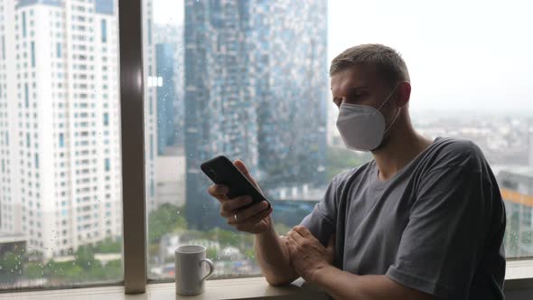 Bored and Lonely White Man in a Face Mask Going Through His Phone While Quarantining