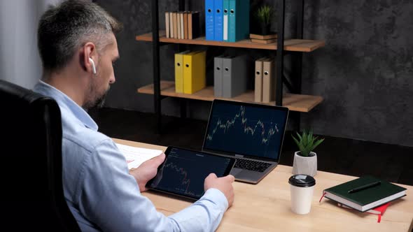 Man Broker Scrolling Tablet with Stock Exchange Chart Laptop with Stock Market