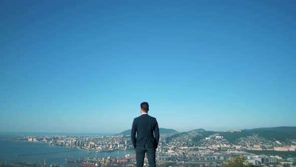 Stylish successful businessman stands on top and looks at the city in the bay from high
